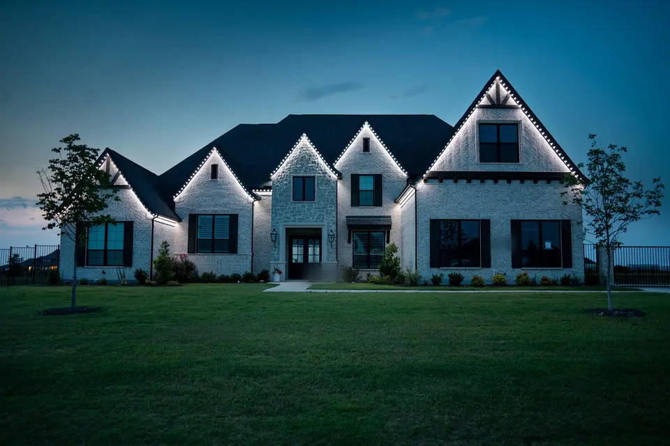 A large white brick house at dusk with a crisp line of white light tracing every gable and eave.