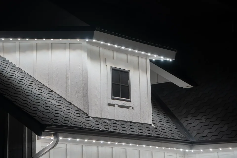Cool white points along an eave and a gable return on a dark shingle roof, close in.