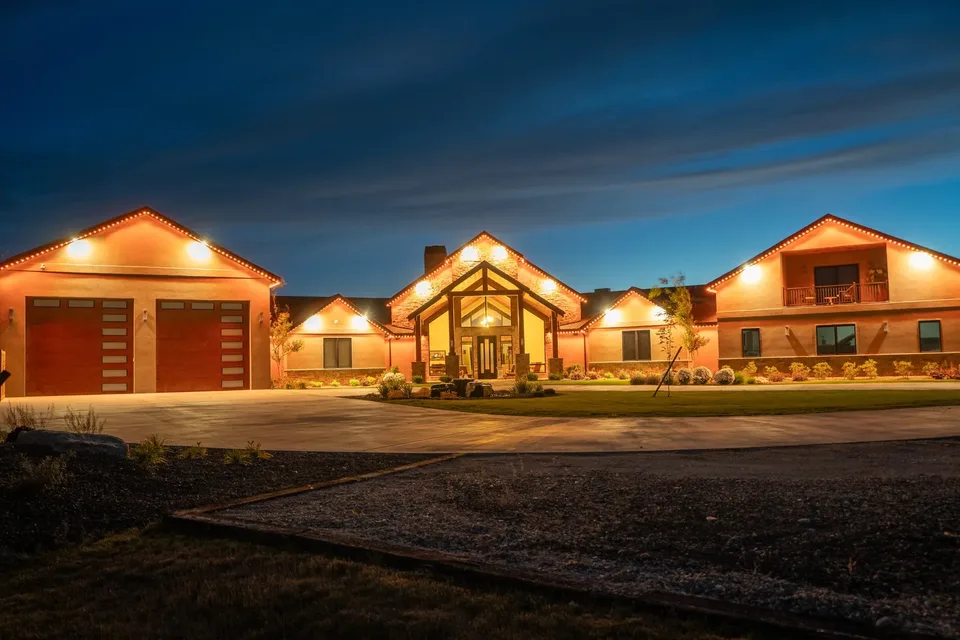 A long ranch estate at dusk, warm light running along the garage gables, the timber entry and both wings from one end of the house to the other.