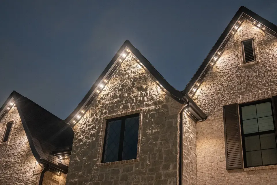 Warm light raking across stone gables on a two-story home after dark.