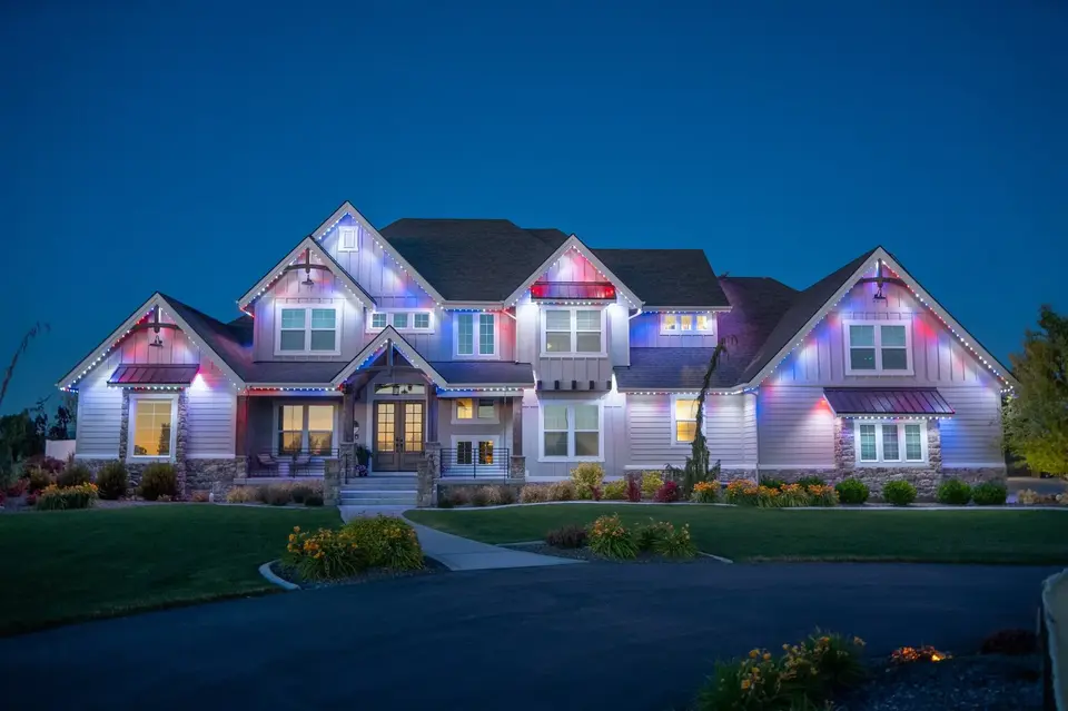 A large two story house at dusk with red, white and blue running along every gable and eave.