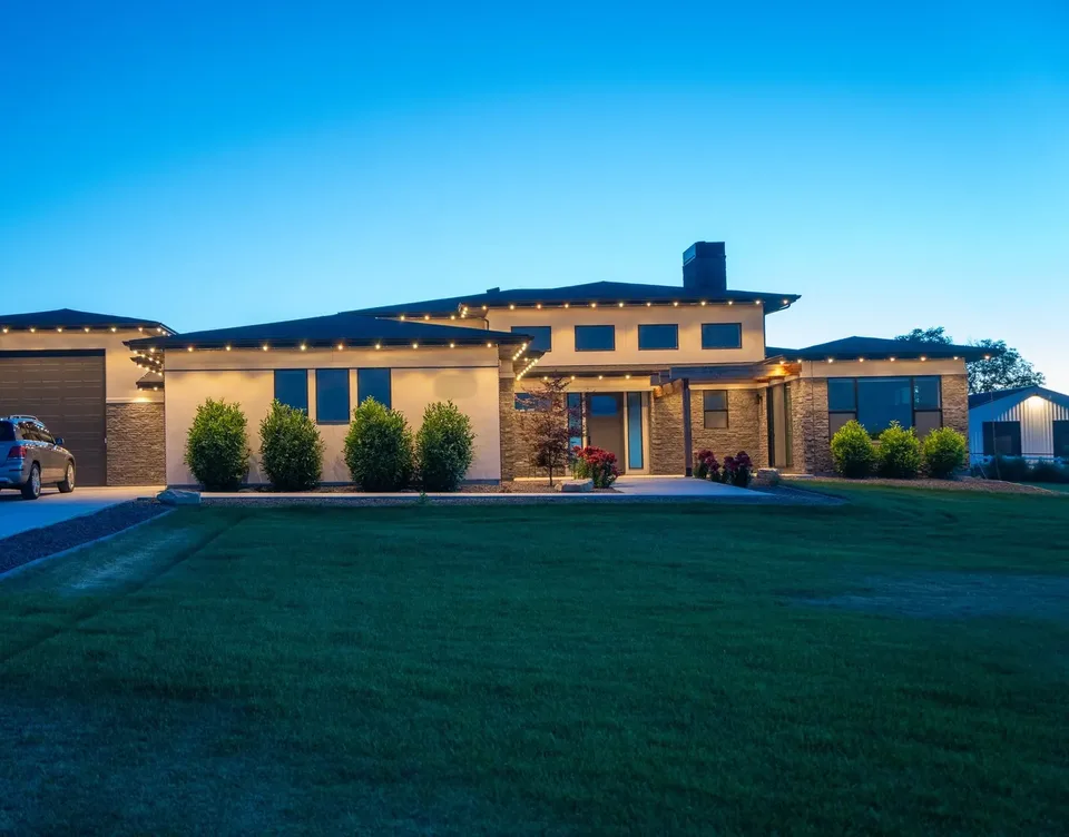 A long single-story house at dusk, a row of warm white points running the full length of its roofline.