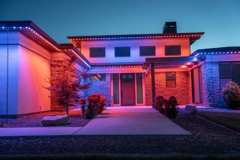 A modern low roofed entry at dusk with the left wall washed red, the eave lines running red at their ends and blue through the middle, and the entry court reading violet where the two meet.