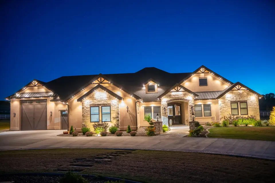 A long estate front at night lit in warm white, the light carried along every eave and gable from one end of the house to the other.