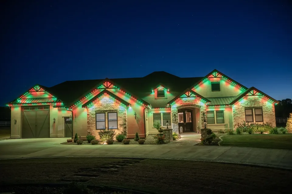 A stone ranch at night with its whole roofline running red and green, the light carried across the garage gable, the front gables and the entry.
