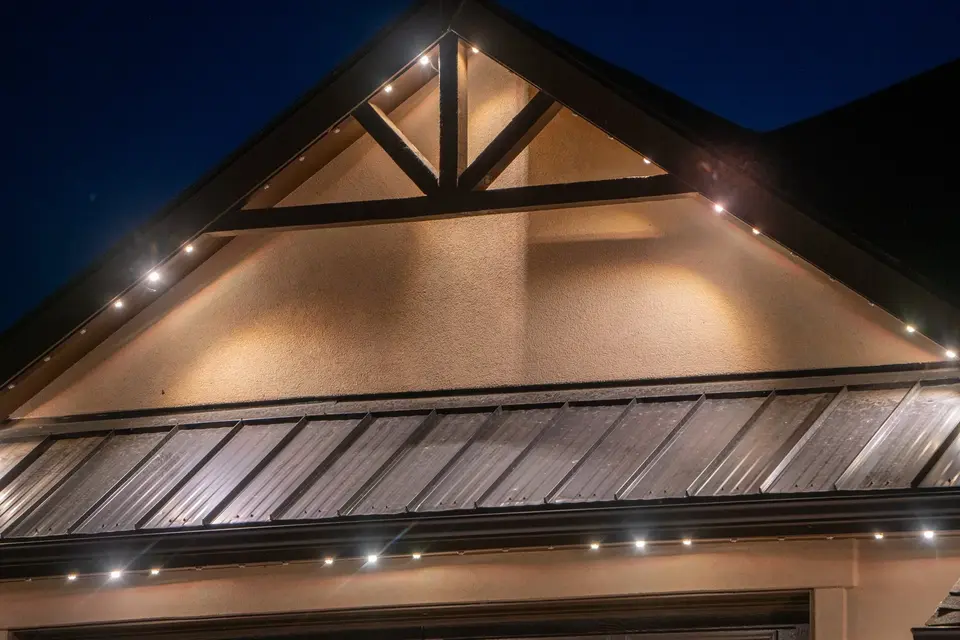 A close night photograph of a gable, with evenly spaced warm points of light running up both roof rakes and along the eave below, washing the gable face.