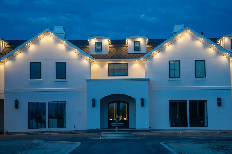 A fountain courtyard below a white stucco estate, the gables in warm white.
