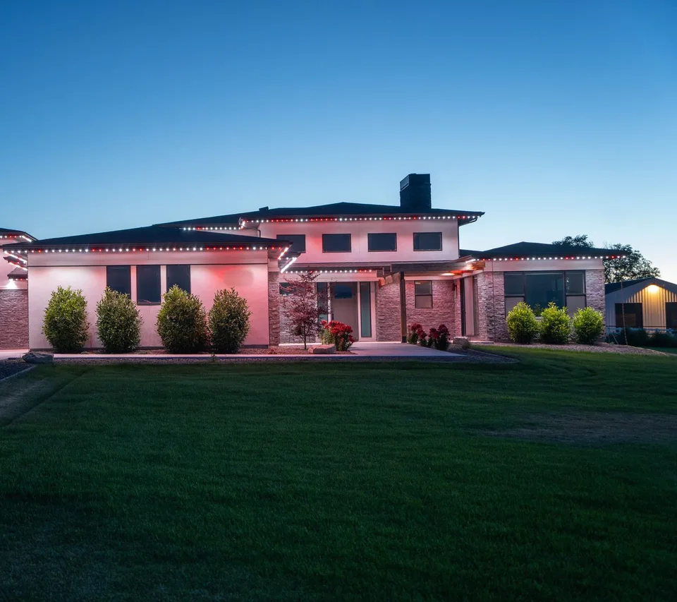 A house seen from the curb at dusk, its roofline lit in red and pink from the garage across to the far gable.